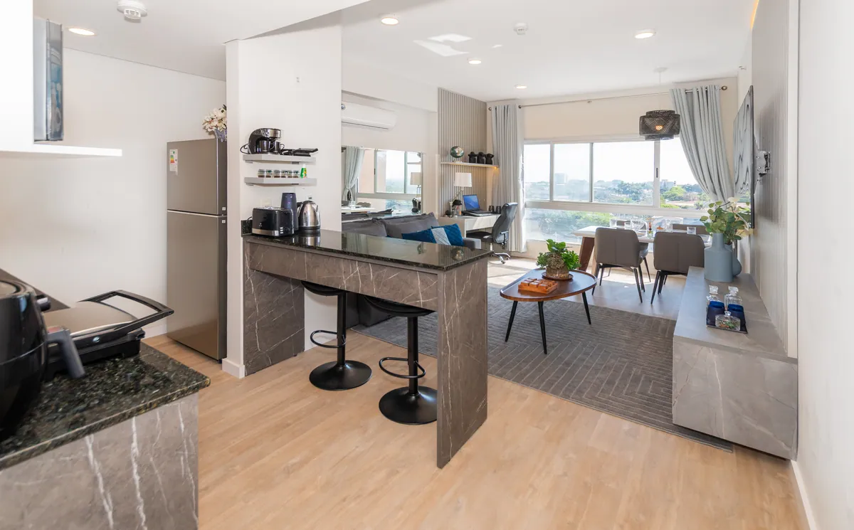 Cocina con la isla y dos banquetas, y el living al fondo